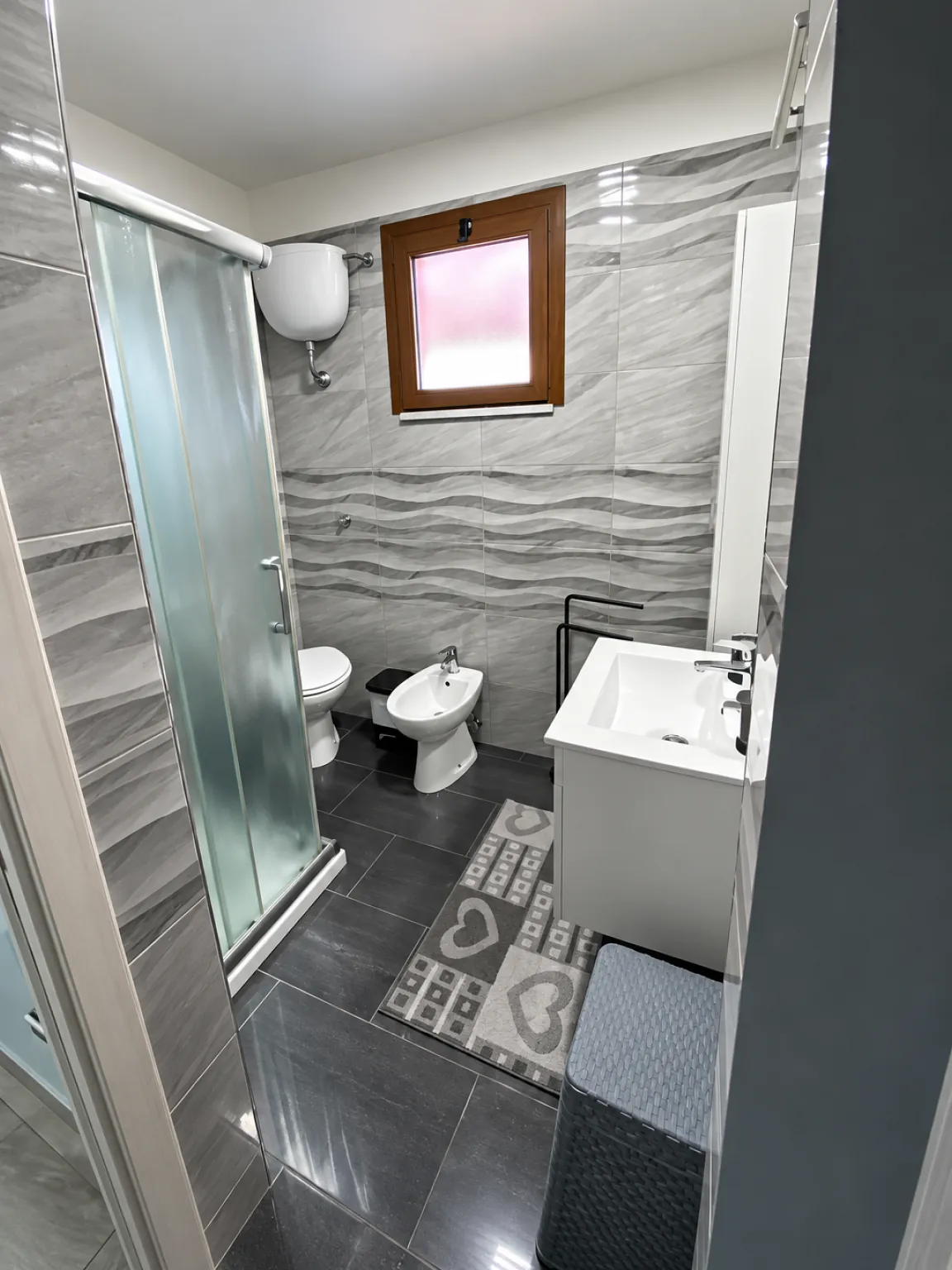Bagno con box doccia, lavabo e piastrelle grigie