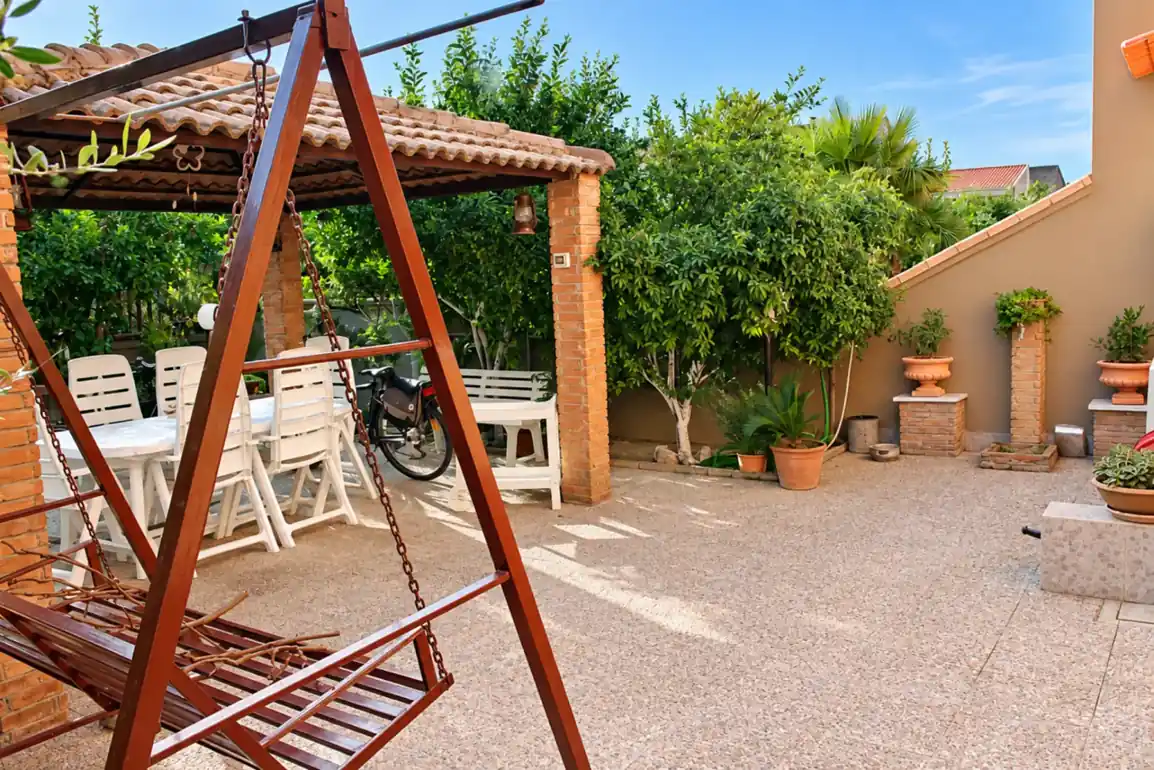Giardino con gazebo in muratura, tavolo da pranzo all'aperto e dondolo